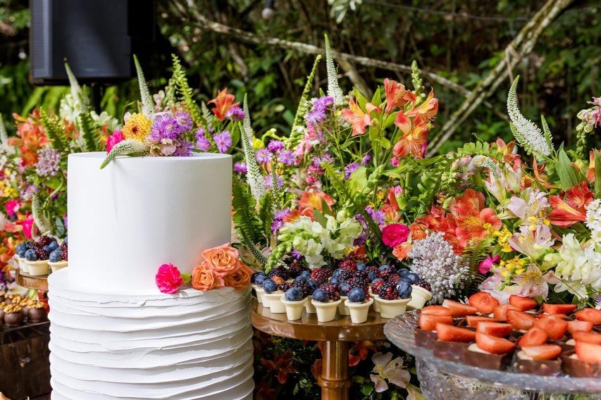 Bolo branco cercado por arranjos de flores coloridas